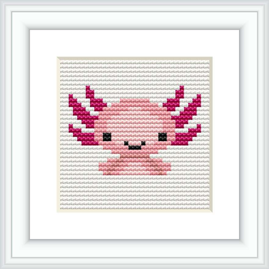 The image displays a square cross stitch pattern featuring a stylized axolotl in a simplistic, cartoonish form. The pattern is predominantly pink with accents in magenta, white, and black, framed within a classic frame, against a white background.