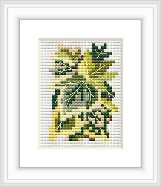 The image showcases a framed cross stitch pattern of various ivy leaves depicted in segments of green and yellow shades. The pattern is set against a white background within a simple frame, highlighting its design.