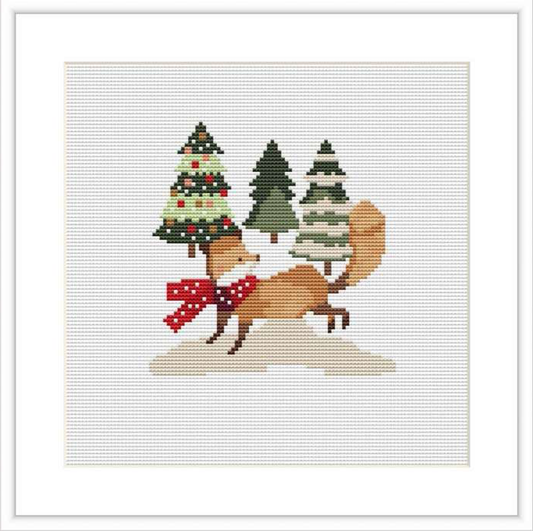 The image shows a cross stitch pattern of a fox with a red and white scarf, positioned in front of a trio of pine trees, one of which is decorated with ornaments. The backdrop is a plain white canvas.