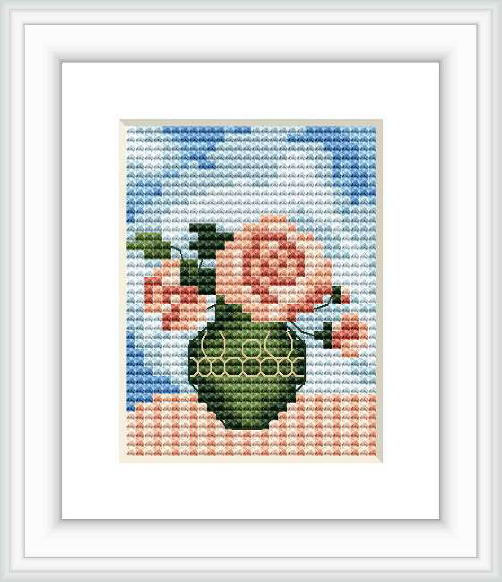 The image displays a framed cross stitch design containing a vase with spring flowers against a sky blue background.
