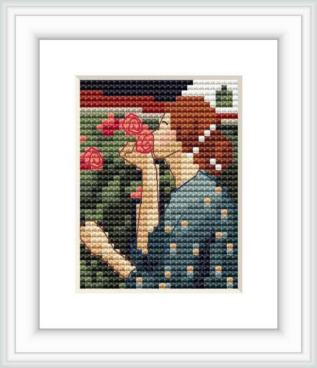 The image depicts a framed cross stitch pattern showing a woman in profile smelling a red rose, surrounded by greenery and other roses.