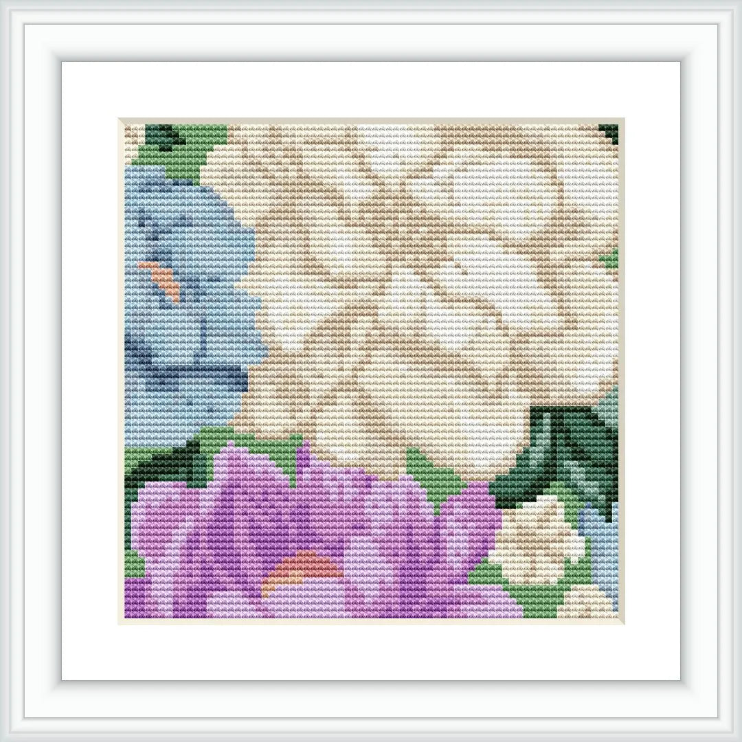 The image displays a framed cross stitch pattern with a beige flower on the top left and a lavender flower on the bottom right. Leaves and stems fill the background around the flowers, with a sky-blue backdrop visible in small portions.