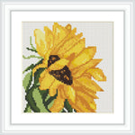 The image depicts a framed cross stitch pattern of a yellow sunflower with brown centers and green leaves against a white background.