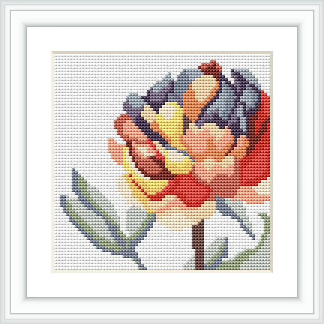 The image displays a framed cross stitch pattern of a single flower with multiple colors. The embroidery is finely detailed on a white canvas, within a simple white frame.