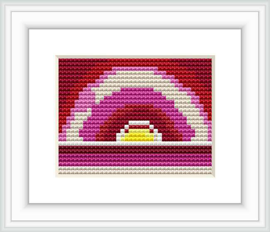 The image shows a framed cross stitch pattern that depicts an abstract sunrise with layered colors fading from dark purple to bright yellow at the center.