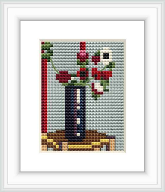 The image depicts a small cross stitch pattern of a still life bouquet of anemones in a vase, placed on a table or flat surface.