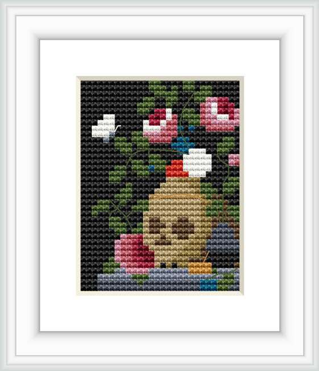 The image showcases a finished cross stitch pattern, featuring a central skull with surrounding elements like flowers, fruits, and books on a dark background.