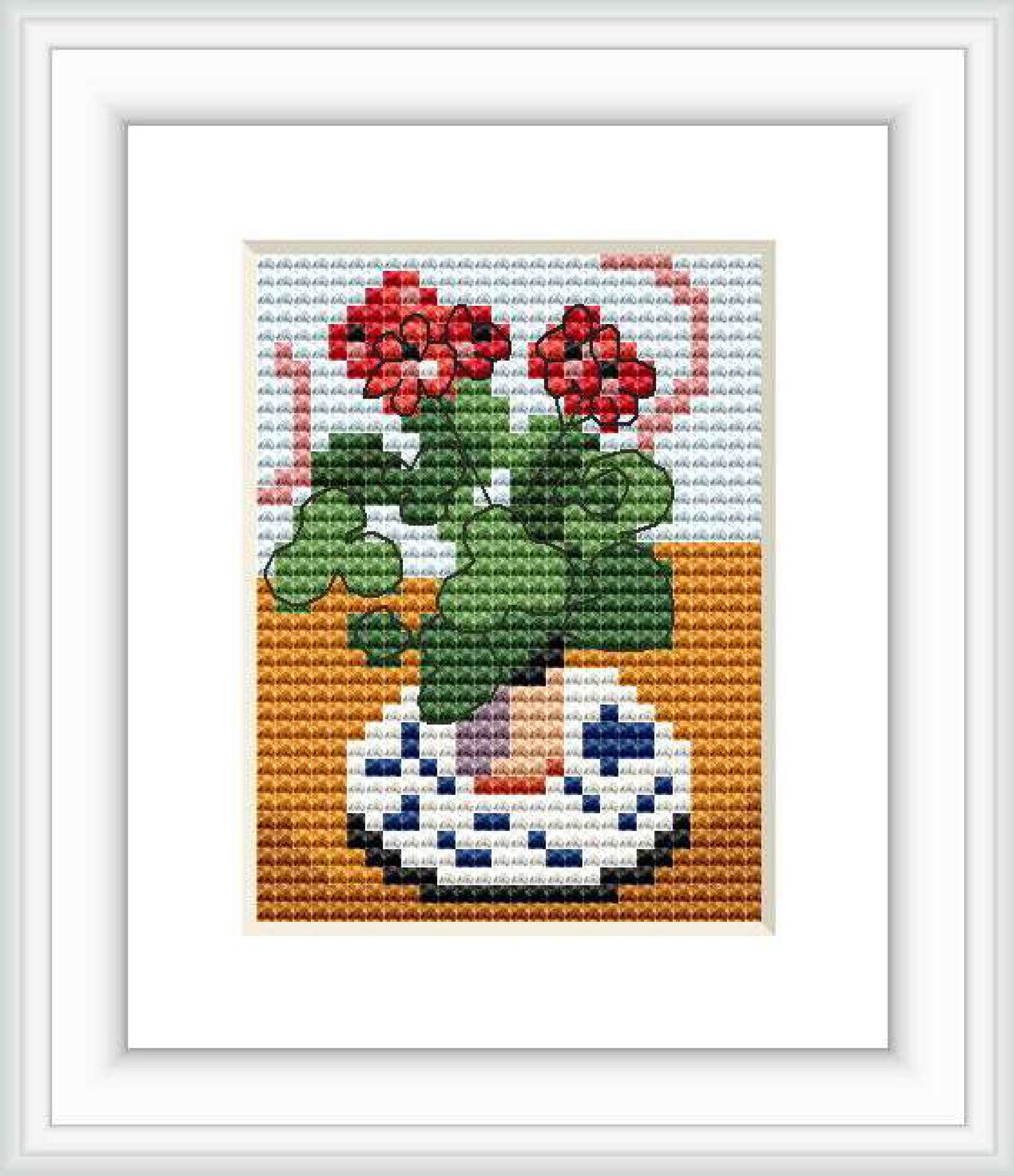 The image depicts a cross stitch pattern of red geraniums in a vase with blue and white patterns, set against an orange and white backdrops.