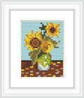 The image depicts a cross stitch pattern of three bright yellow sunflowers in a vase, against a two-toned background with a light blue sky and brown tabletop.