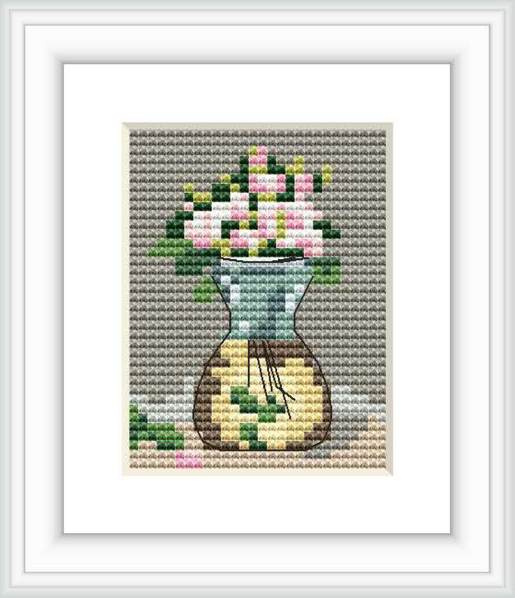 The image depicts a cross stitch pattern featuring a vase with blooming roses. The surface on which the vase rests is partially visible, and the background consists of a textured gray fabric.