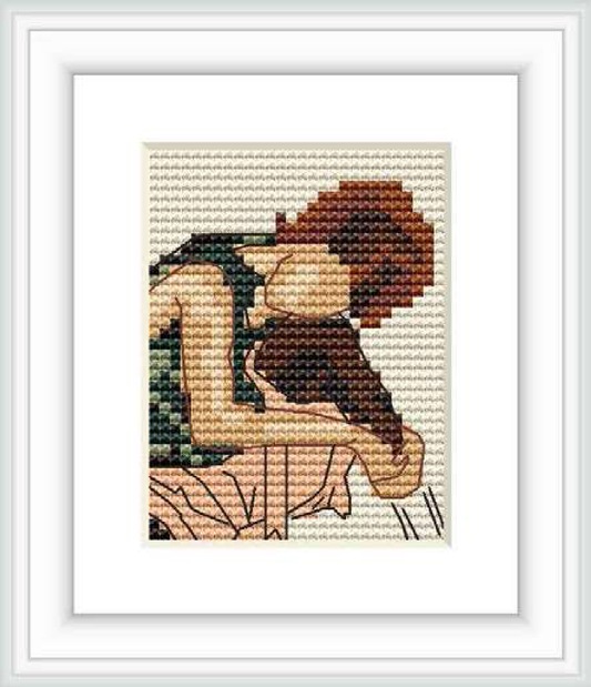 The image showcases a framed cross stitch pattern with the representation of a seated figure from the back, its arms wrapped around the knees, set against a background of pattern-textured stitches.