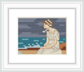The cross stitch pattern depicts a female figure sitting by the sea, the horizon visible in the background with soft waves, under a gradient sky from dark to light blue tones.