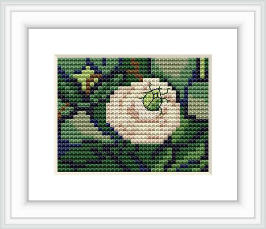 The image shows a framed cross stitch pattern featuring a central pinkish-white rose with a small beetle on top, set against a background of green foliage with hints of blue and purple.