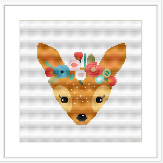 The image depicts a cross stitch pattern of a deer's head with a crown of colorful flowers on its head. The deer is centered against a white background, with a subtle grid visible indicating the pattern's design.