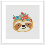 The image showcases a completed cross stitch pattern featuring a cute sloth with a contented expression. The sloth is decorated with a crown of flowers and berries on its head, centered on a white background.