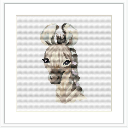 The image features a framed cross stitch pattern of a baby zebra head with a simple color palette, centered on a white background and enclosed within a square border.