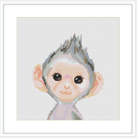 The image showcases a framed cross stitch pattern on a white background. The pattern is a stylized depiction of a baby monkey with oversized ears and an expression of playful innocence.