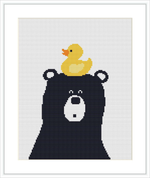 The image features a cross stitch pattern depicting the head of a black bear looking straight ahead, with open eyes and a rounded snout. On top of the bear's head sits a small yellow rubber duck, facing towards the viewer.