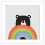 The image displays a cross stitch pattern featuring a black bear with a simple expression. The bear is seen peeking over a large, colorful rainbow that fills the lower half of the frame. The background is plain white.