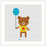 The image depicts a cross stitch pattern of a cute brown bear standing upright, holding a turquoise balloon with its right paw. The bear is wearing a yellow shirt with a red star in the middle. There is a small green stitch that could represent a patch of grass at the bottom.