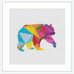 The image showcases a cross stitch pattern of a bear profile filled with various vibrant, geometric shapes resembling a low-poly design, framed in white and displayed on a flat surface.