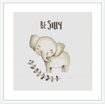 The image depicts a simplistic cross stitch design of a playful elephant standing on its hind legs. Above the elephant is the phrase 'Be Silly' in stylized text. The pattern is centered on an ivory-colored Aida fabric background.