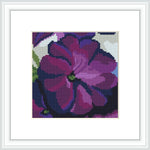 The cross-stitch pattern depicts a close-up of petunia flowers, predominantly in shades of purple and lavender, with hints of green leaves and a contrasting black background, all framed by a simple white border within the image.