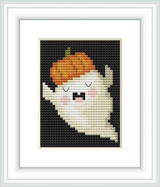 The image displays a framed cross stitch pattern of a cute ghost with a pumpkin on its head. The background is black, and the ghost is primarily white with orange, grey, and blush accents.