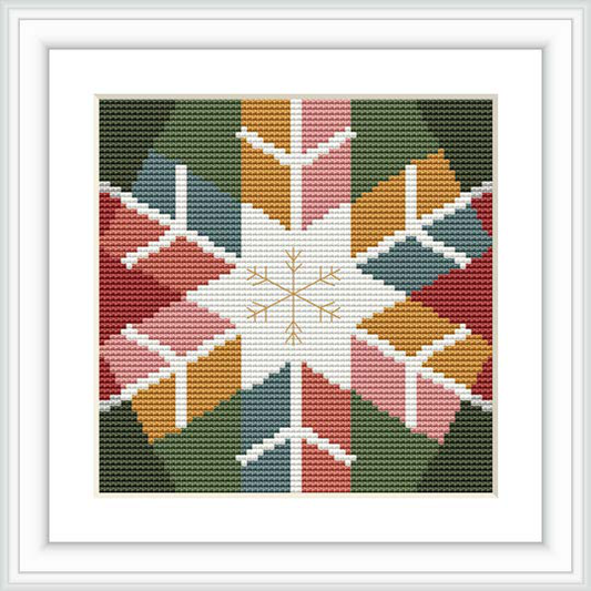 The image displays a framed cross stitch pattern featuring a central snowflake motif surrounded by geometric shapes and winter colors.