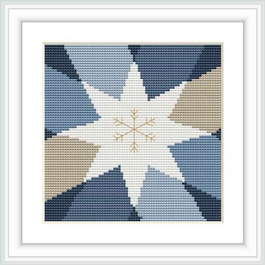 The image shows a framed cross stitch pattern featuring a central geometric star shape with points extending outward. The star is framed by four shades: white, gold, and two shades of blue. The overall aesthetic has a clean and festive look.