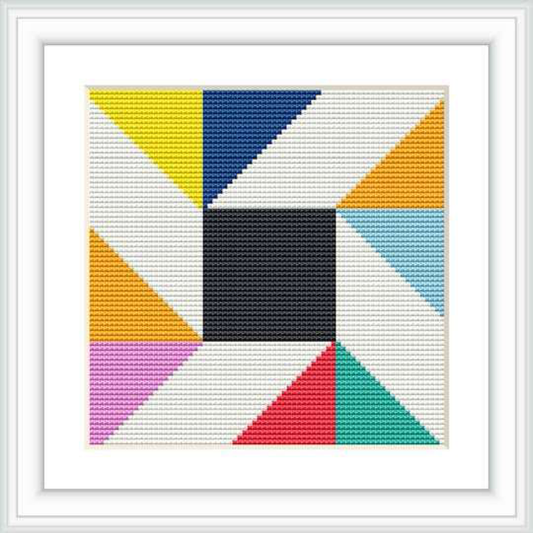 The image shows a framed cross stitch pattern featuring a central black square surrounded by triangles and blocks of different colors, creating a geometric design.