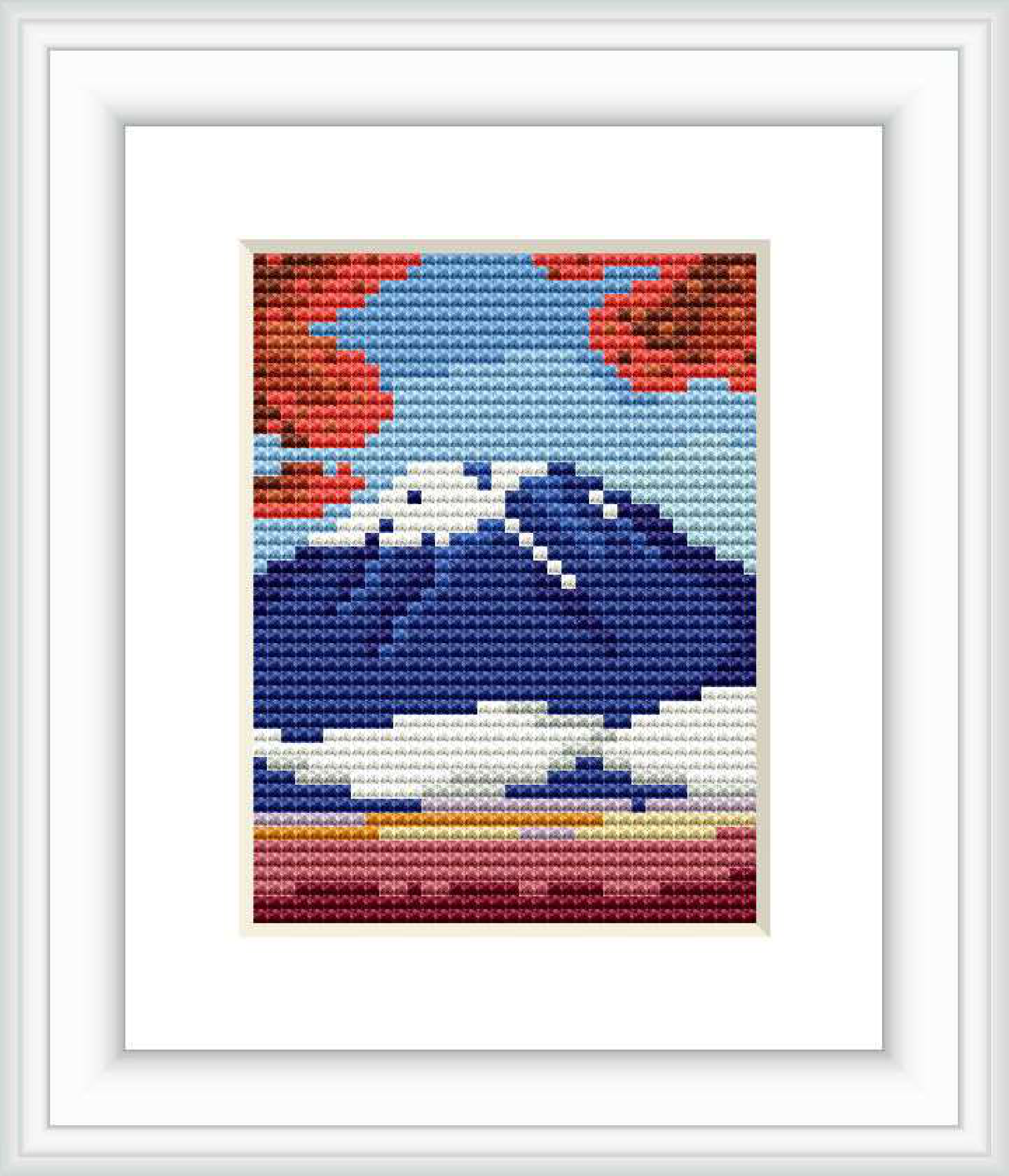 The image depicts a cross stitch pattern framed and displayed on a wall. The pattern showcases a stylized mountain landscape with a large mountain in the center, sky above, and striped foreground suggesting land or water.