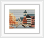 The image depicts a cross stitch pattern showcasing a tranquil urban landscape scene. It features historic European buildings with prominent roofs and a bridge over a calm waterway, presented in a charming, pixelated style.