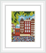 This image depicts a framed cross stitch pattern representing a scene with Amsterdam canal houses. The houses are detailed with multiple windows and the pattern includes elements such as water, a canal, and a tree-dotted skyline.