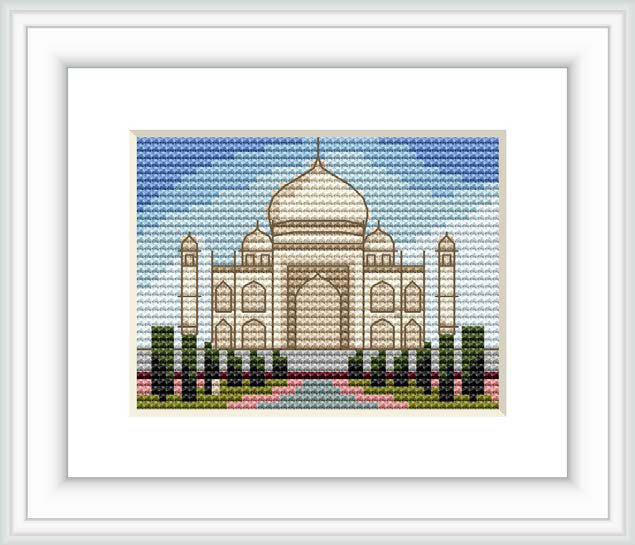 The image depicts a cross stitch pattern of the Taj Mahal framed in white, against a blue sky. The monument is represented with beige and white stitches, surrounded by greenery and small pink accents, suggesting a garden.