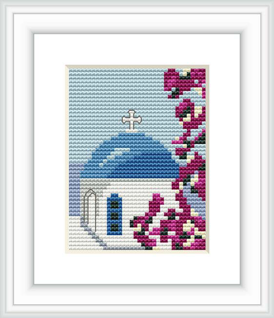 The image depicts a cross stitch pattern portraying a white building with a classic Santorini blue dome and a cross at the top. To the right, there is a branch with pink bougainvillea flowers. The background suggests a clear sky.