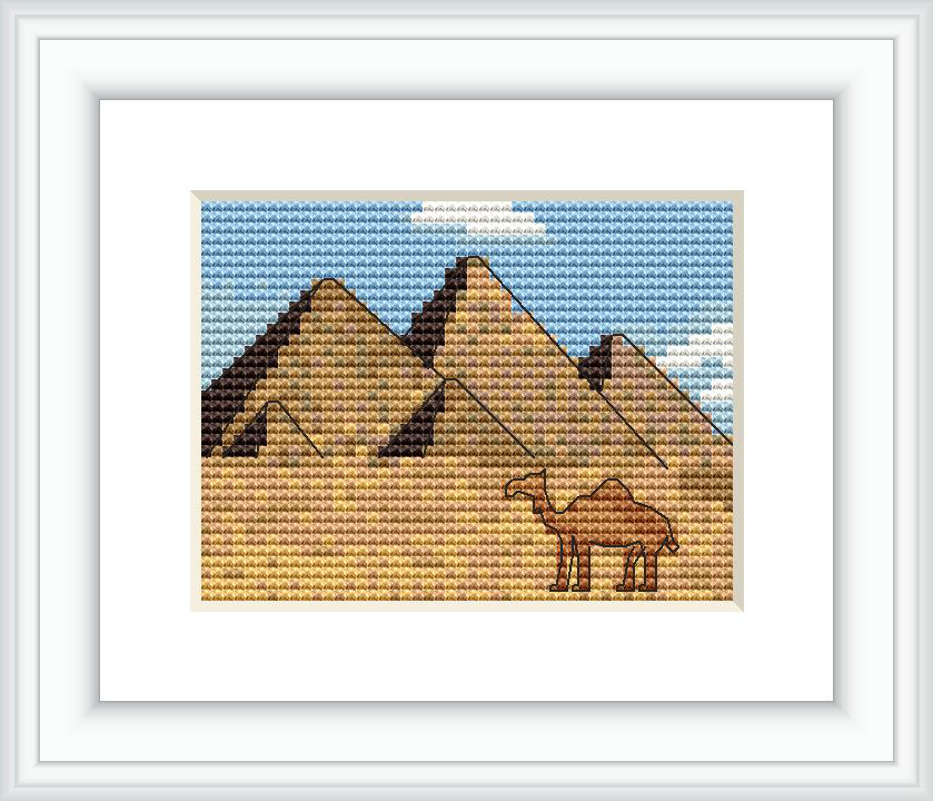 The image depicts a cross stitch pattern with the three Great Pyramids of Giza in the background. In the foreground, there is a camel. The setting appears to be a desert, with a clear sky.