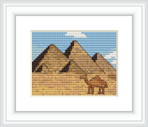 The image depicts a cross stitch pattern with the three Great Pyramids of Giza in the background. In the foreground, there is a camel. The setting appears to be a desert, with a clear sky.