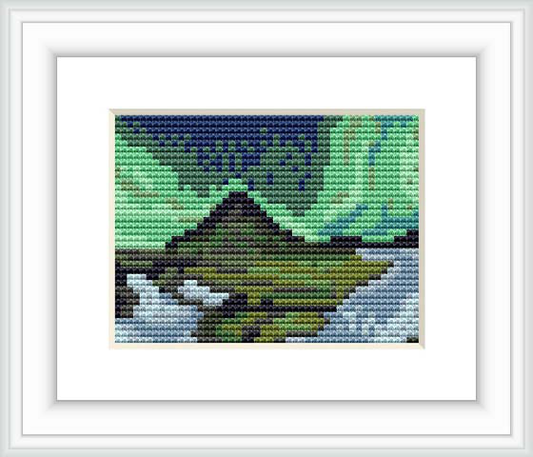 The image shows a framed cross stitch pattern depicting a stylized mountainous Iceland landscape, with dominant hues of blues and greens resulting in a pixelated nature scene.