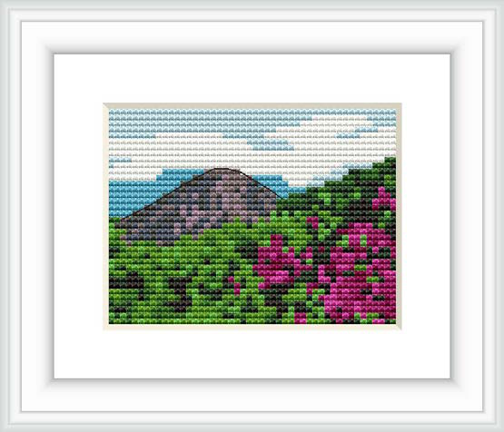 The image depicts a cross-stitch pattern framed in white, showing a mountain landscape with vibrant pink flora in the foreground, a grey mountain in the middle, and a blue and white sky.