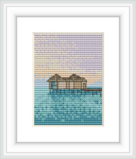 The image shows a framed cross stitch pattern of an overwater hut on stilts, set against a gradient sunset sky that transitions to a calm ocean's surface.