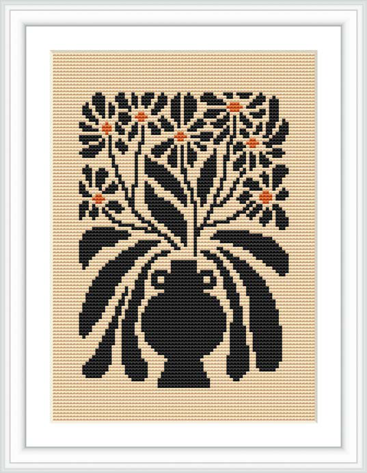 The image shows a framed cross-stitch pattern depicting a bouquet of flowers in a vase, predominantly in black with cream background and orange-tinted accents.