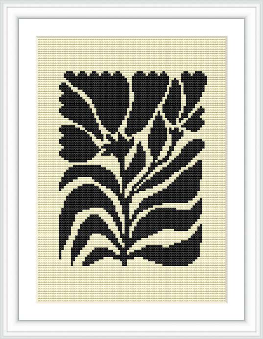 The image depicts a cross stitch pattern framed in a simple white frame. The pattern itself is a stylized representation of flowers in black thread on a cream or white canvas fabric. It's displayed against a flat, neutral background.