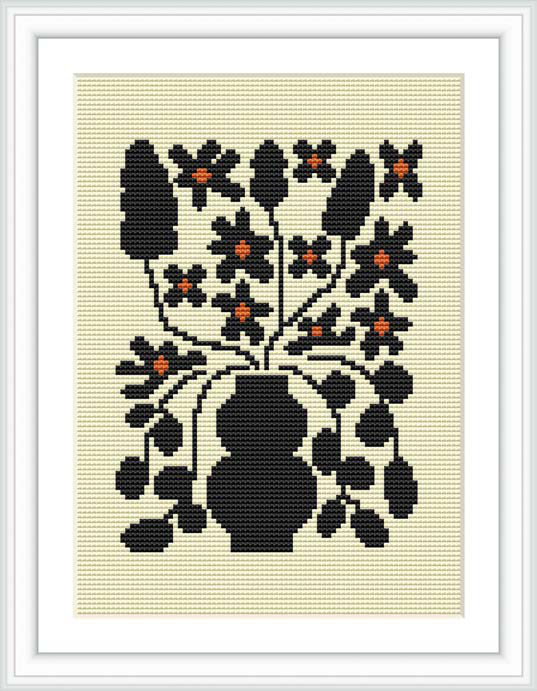 The image features a framed cross stitch pattern of a stylized black floral design with orange and black flowers, set against a cream background.