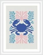 The image features a framed cross stitch pattern of a stylized crab centered on a white fabric. Surrounding the crab are coral-like embellishments in various shades of blue, pink, and coral. The pattern is rendered with a variety of stitches to depict the distinct form of the crab and the decorative elements.