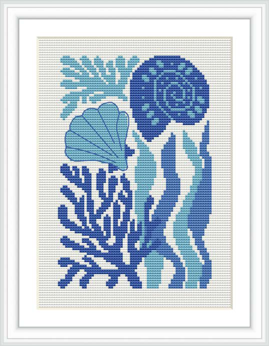 The image displays a cross stitch pattern featuring ocean-inspired motifs. The design includes various types of seashells, coral-like elements, and seaweed shapes arranged in a pleasing composition. The pattern illustrates a gradient in blue tones ranging from light aqua to navy against a white background, framed in a simple white square frame.