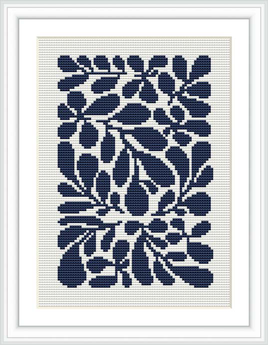 The image depicts a framed cross stitch design featuring a monochromatic floral pattern in various shades of blue, set against a white fabric background.