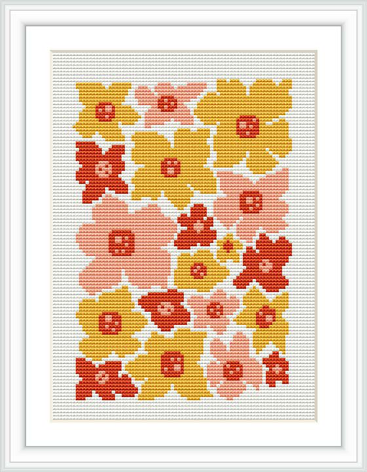 The image displays a cross stitch pattern of stylized flowers in shades of pink, red, yellow, and accents of white, all set against a cream background. The pattern is framed with a simple white border, suggesting a completed and framed project.