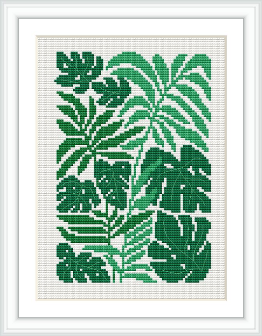 The image shows a framed cross stitch pattern featuring a design of Monstera plant leaves. The leaves are in various shades of green with a white background, and the pattern presents a pixelated style typical of cross stitching.