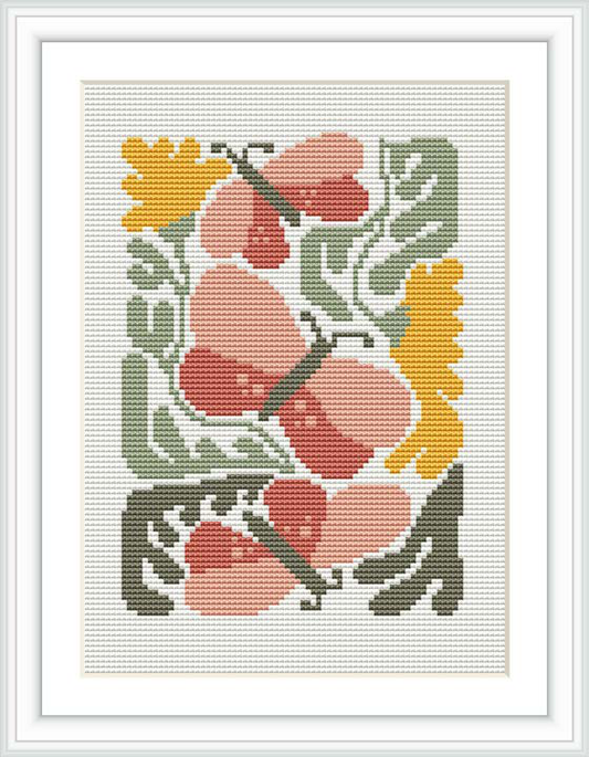 The image shows a framed cross stitch design with a floral pattern featuring coral blossoms and green leaves on a cream-colored canvas.